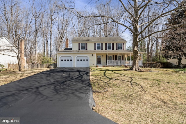 colonial-style house with fence, driveway, a porch, an attached garage, and a front lawn