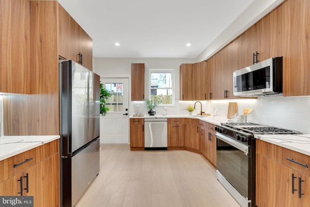 kitchen featuring appliances with stainless steel finishes, tasteful backsplash, sink, light hardwood / wood-style floors, and light stone countertops