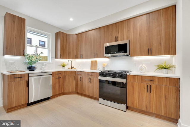 kitchen with tasteful backsplash, appliances with stainless steel finishes, sink, and light hardwood / wood-style flooring