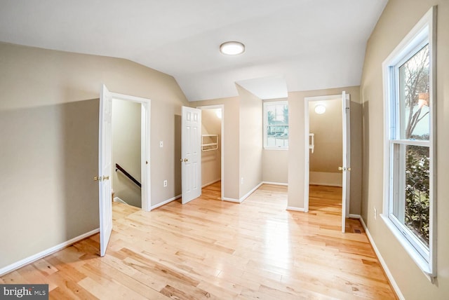 unfurnished bedroom with a spacious closet, vaulted ceiling, and light wood-type flooring