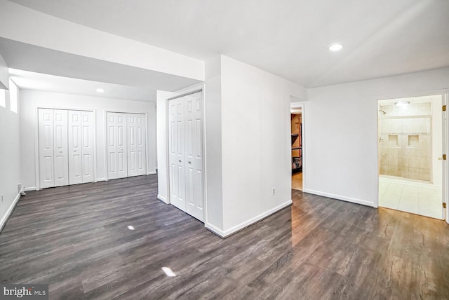 unfurnished bedroom featuring ensuite bathroom, dark hardwood / wood-style flooring, and two closets