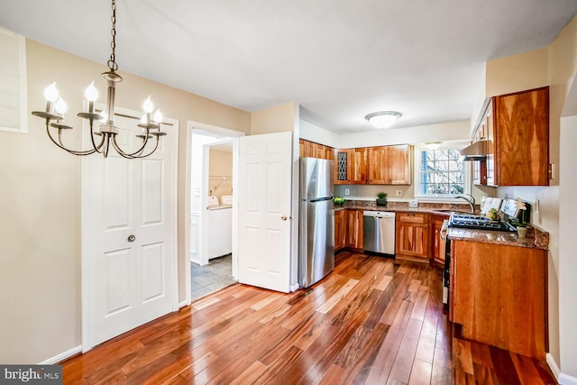 kitchen featuring pendant lighting, dark stone countertops, a chandelier, hardwood / wood-style flooring, and stainless steel appliances