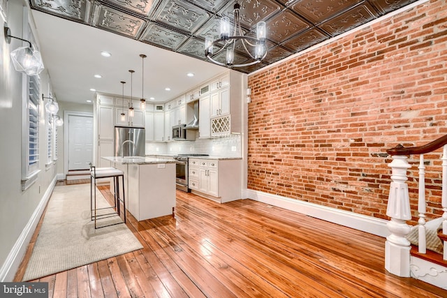 kitchen with a breakfast bar, appliances with stainless steel finishes, pendant lighting, brick wall, and a kitchen island with sink