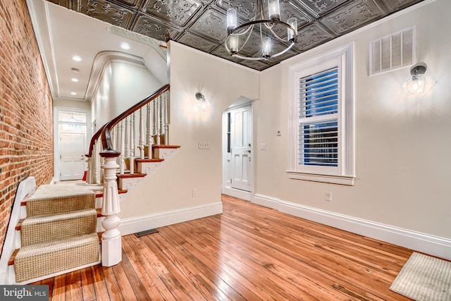 entrance foyer with crown molding, light hardwood / wood-style flooring, a chandelier, and brick wall