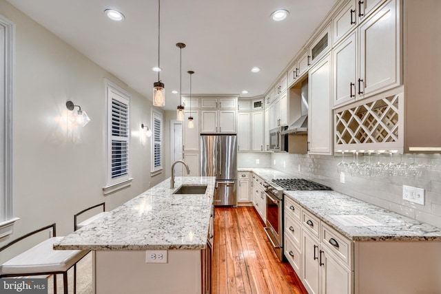 kitchen with a center island with sink, stainless steel appliances, backsplash, a sink, and light wood-type flooring