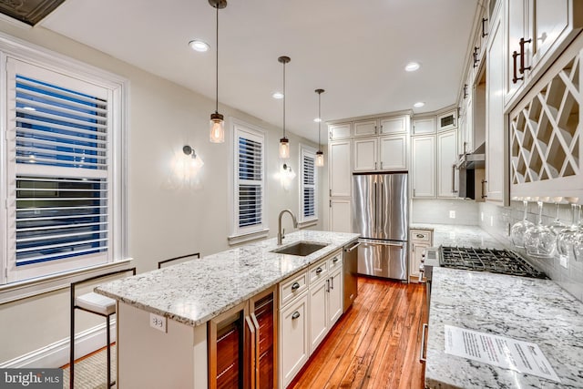 kitchen featuring decorative backsplash, appliances with stainless steel finishes, light wood-style floors, a sink, and light stone countertops