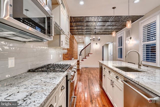 kitchen featuring sink, backsplash, stainless steel appliances, light stone countertops, and decorative light fixtures