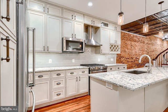 kitchen with wall chimney exhaust hood, sink, pendant lighting, stainless steel appliances, and light stone countertops