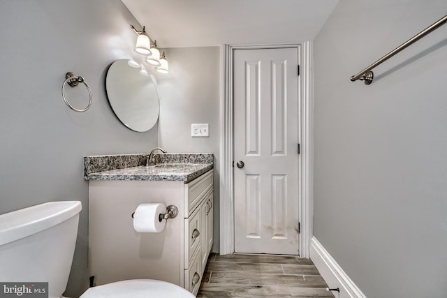 half bath with toilet, wood tiled floor, baseboards, and vanity