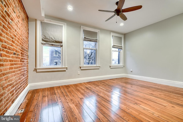 unfurnished room with brick wall, wood-type flooring, a ceiling fan, and baseboards