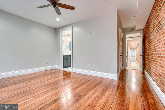 spare room with brick wall, hardwood / wood-style floors, and ceiling fan