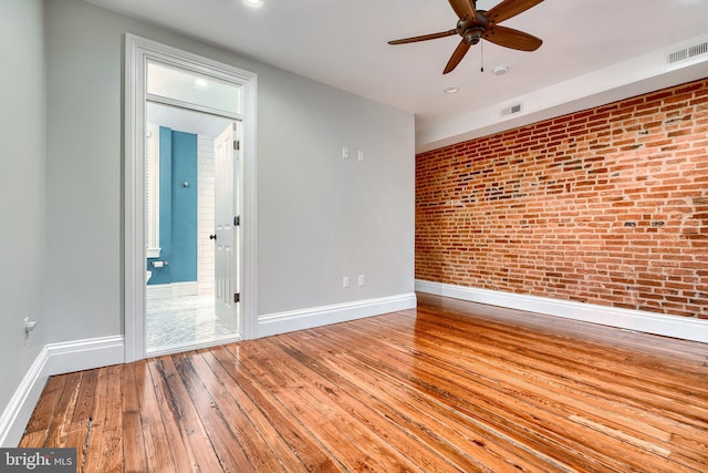 spare room with wood-type flooring, baseboards, visible vents, and brick wall