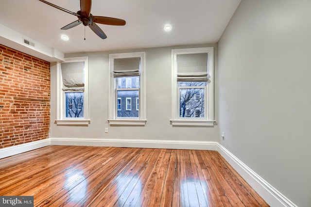 empty room featuring brick wall, hardwood / wood-style flooring, visible vents, and baseboards