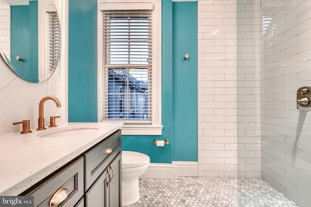 full bathroom with toilet, baseboards, a tile shower, and vanity