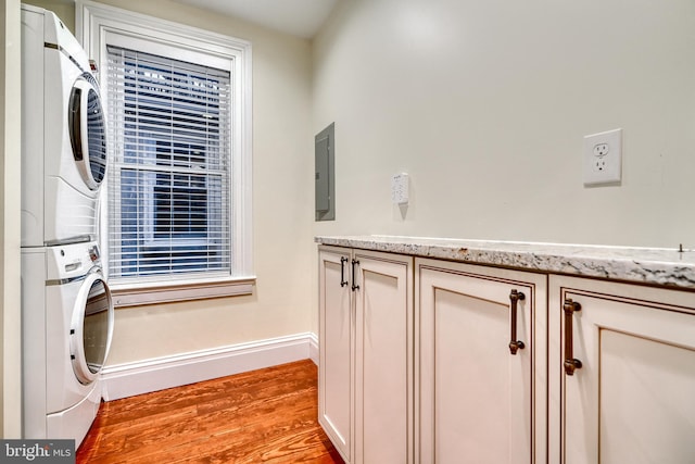 laundry area with light wood-style flooring, baseboards, stacked washing maching and dryer, cabinet space, and electric panel