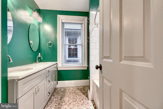 bathroom featuring double vanity, a healthy amount of sunlight, a sink, and baseboards