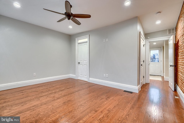 spare room featuring ceiling fan, brick wall, and light hardwood / wood-style floors