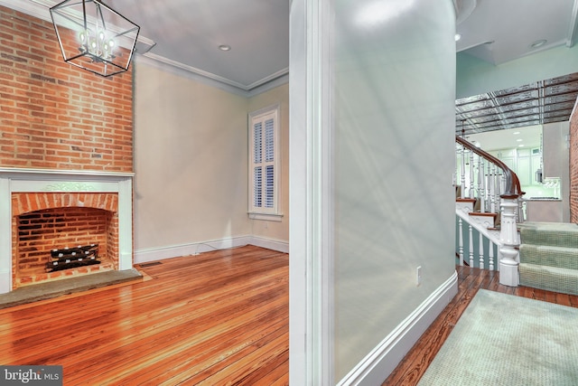 interior space featuring ornamental molding, a brick fireplace, wood-type flooring, and baseboards