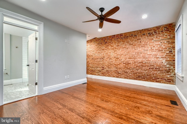 empty room featuring wood-type flooring, brick wall, and ceiling fan