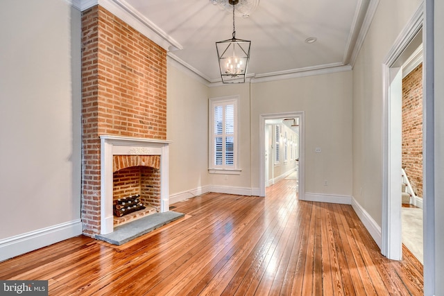 unfurnished living room featuring baseboards, wood-type flooring, ornamental molding, a brick fireplace, and a chandelier