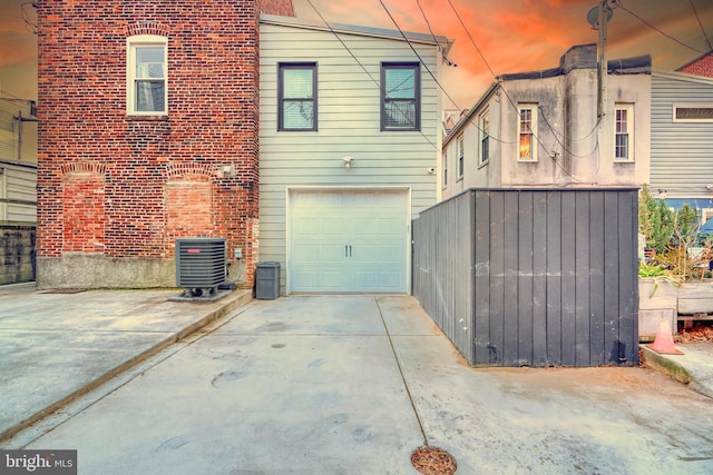 back house at dusk with central AC unit and a garage