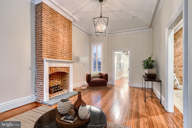 living room featuring an inviting chandelier, crown molding, a fireplace, and light wood-type flooring