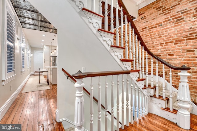 stairs with a towering ceiling, hardwood / wood-style flooring, brick wall, and baseboards