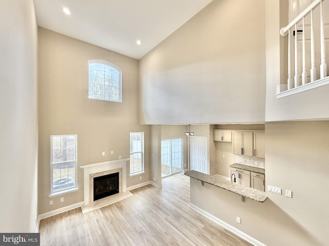 unfurnished living room featuring a premium fireplace, high vaulted ceiling, and light hardwood / wood-style floors