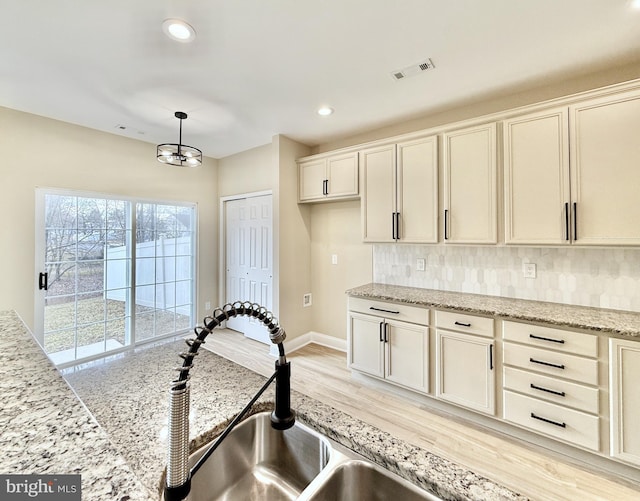 kitchen featuring light stone counters, decorative light fixtures, and light hardwood / wood-style flooring