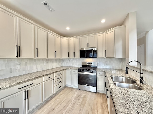 kitchen featuring sink, light stone counters, light hardwood / wood-style flooring, stainless steel appliances, and backsplash