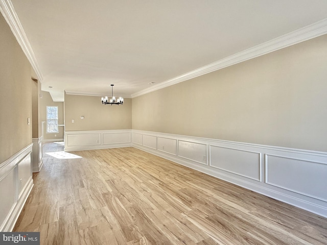 spare room featuring an inviting chandelier, crown molding, and light wood-type flooring