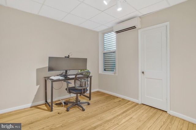 home office featuring a paneled ceiling, a wall mounted AC, and light hardwood / wood-style flooring