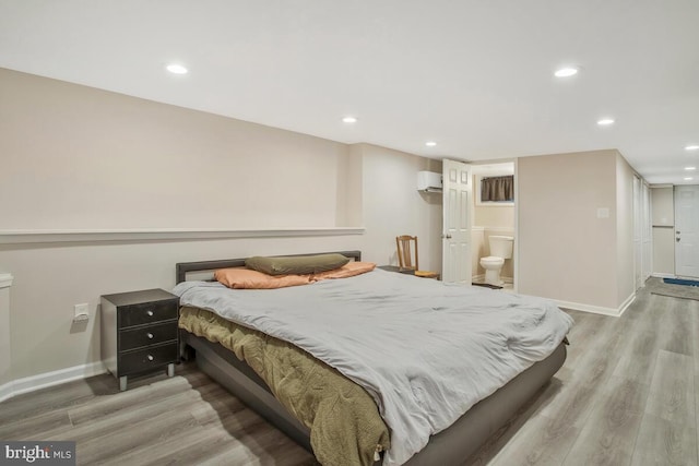 bedroom featuring connected bathroom, wood-type flooring, and a wall mounted AC