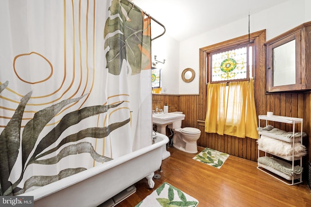 bathroom with hardwood / wood-style flooring, toilet, a bathing tub, and wood walls