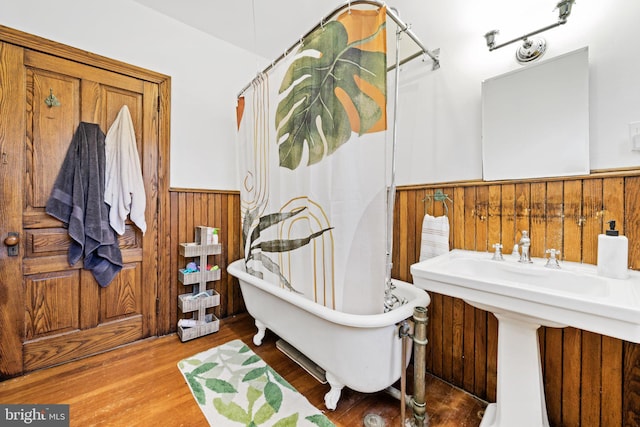 bathroom featuring a bathing tub, sink, hardwood / wood-style floors, and wooden walls