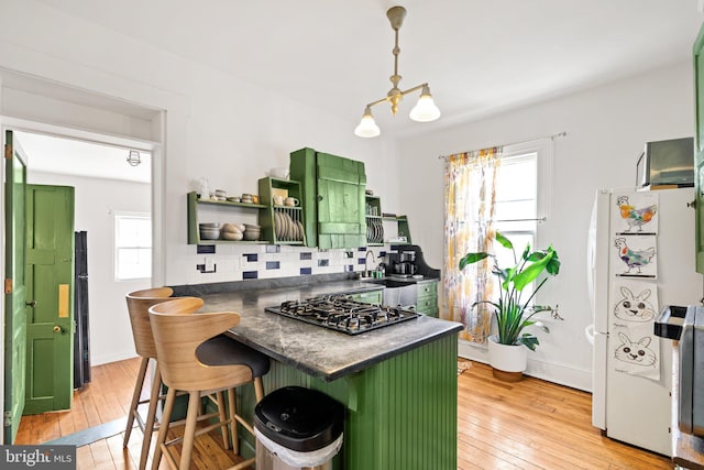 kitchen featuring a breakfast bar, stainless steel gas stovetop, white refrigerator, green cabinets, and light wood-type flooring