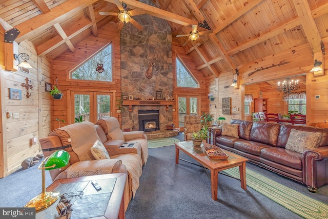 carpeted living room with beamed ceiling, wood walls, ceiling fan with notable chandelier, wooden ceiling, and a fireplace