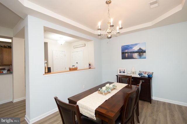 dining room with an inviting chandelier, wood-type flooring, and a raised ceiling