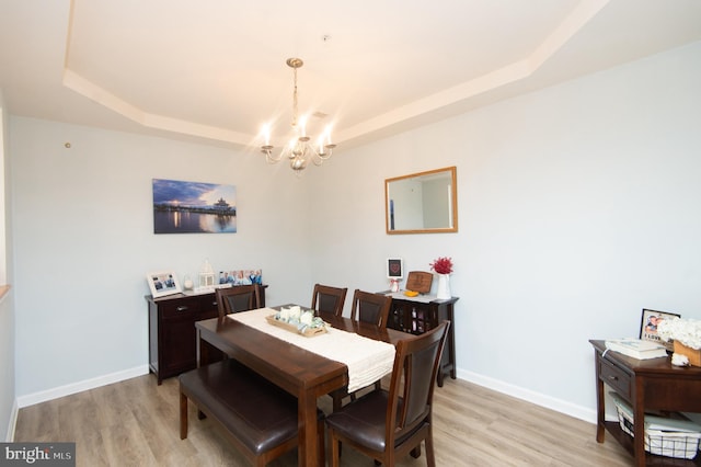 dining room featuring an inviting chandelier, light hardwood / wood-style floors, and a raised ceiling