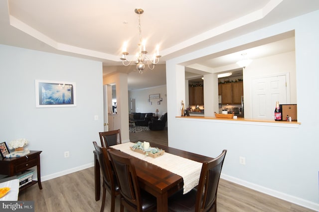 dining area featuring wood-type flooring, a chandelier, and a tray ceiling