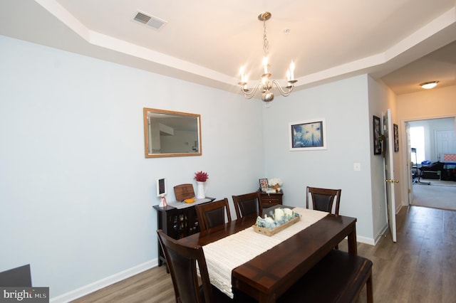 dining space featuring a notable chandelier, a tray ceiling, and wood-type flooring