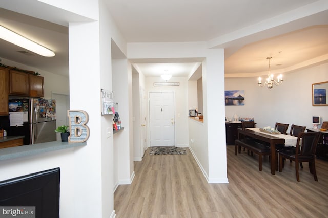 interior space with light hardwood / wood-style flooring, hanging light fixtures, a notable chandelier, and stainless steel fridge