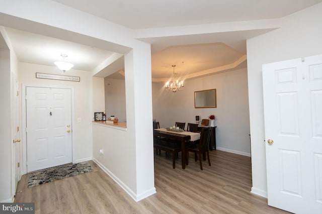 foyer entrance featuring an inviting chandelier, a raised ceiling, and light hardwood / wood-style floors