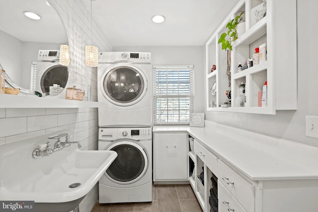 laundry area with tile walls, stacked washer and dryer, cabinets, and sink