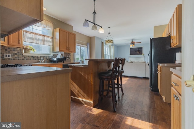 kitchen featuring a kitchen bar, stainless steel gas cooktop, tasteful backsplash, hanging light fixtures, and dark hardwood / wood-style floors