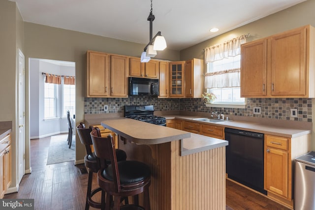 kitchen featuring sink, a center island, a kitchen breakfast bar, pendant lighting, and black appliances