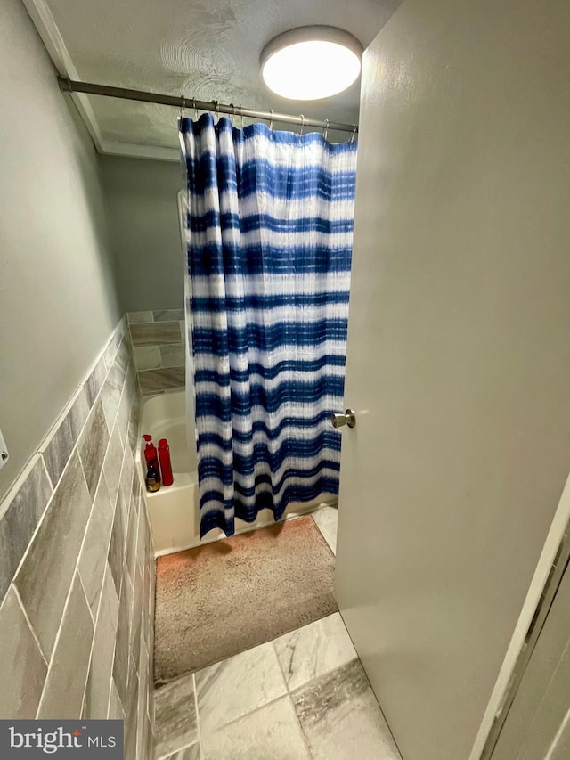 bathroom with tile walls and shower / bath combo with shower curtain