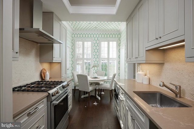 kitchen with sink, stainless steel gas range oven, ornamental molding, a tray ceiling, and wall chimney range hood