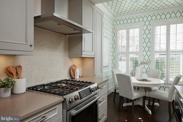 kitchen featuring light countertops, dark wood-type flooring, gas stove, wall chimney range hood, and wallpapered walls