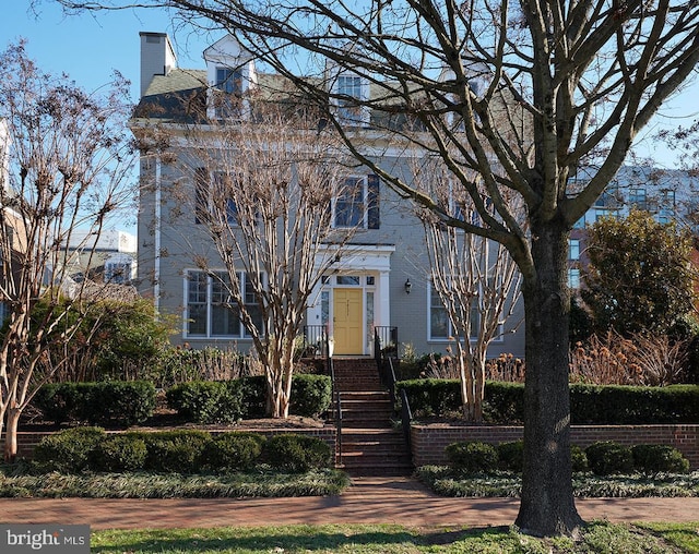 view of front facade featuring stairway, brick siding, and a chimney